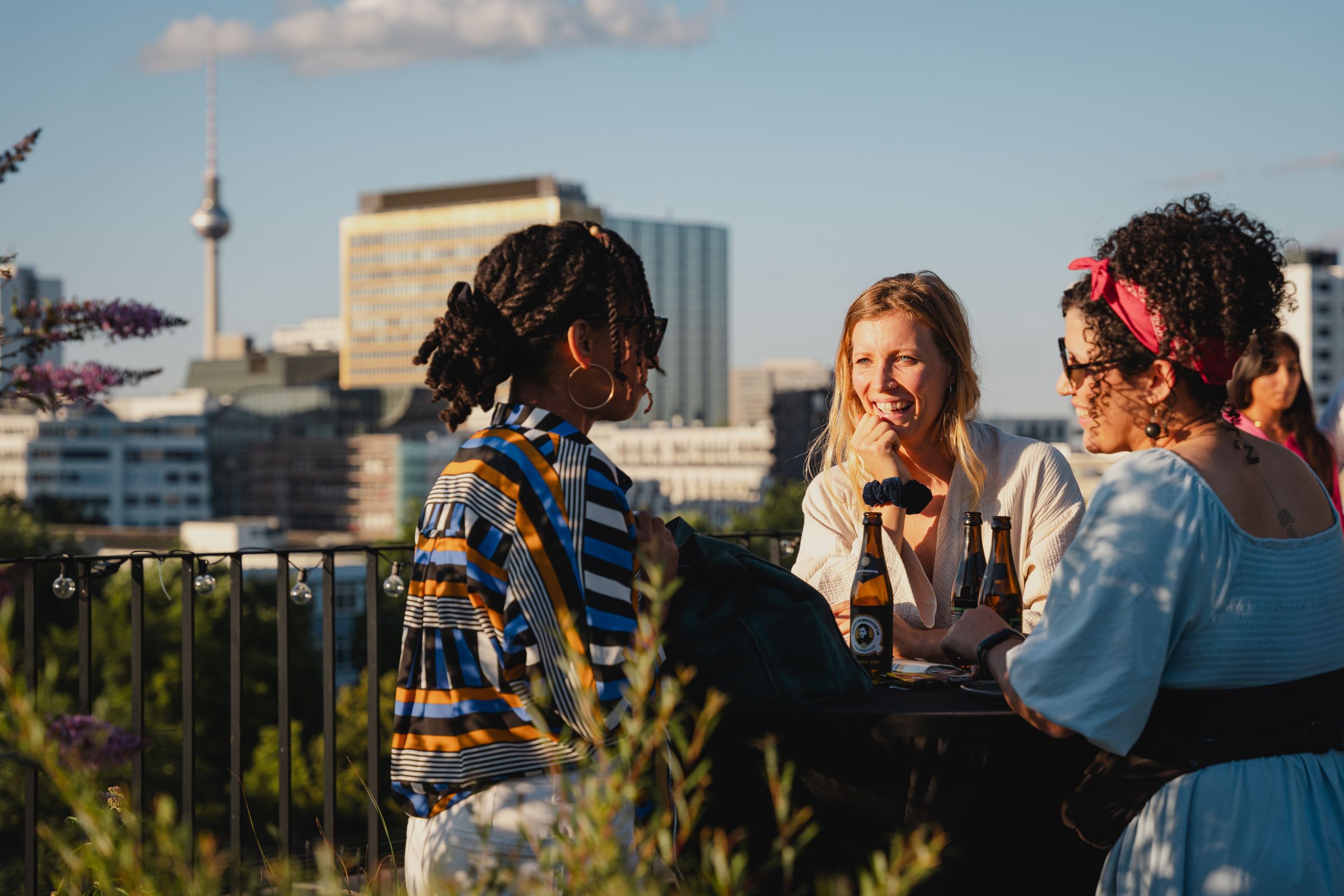 Drei Frauen im Gespräch auf einer Dachterrasse mit Blick auf die Berliner Skyline